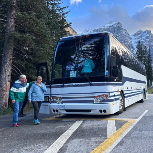 Couple walking to their tour bus with mountains in the background
